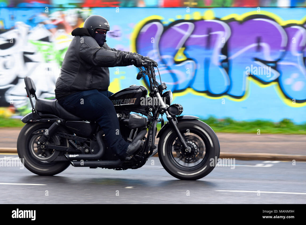 Fat obese motorcycle rider riding past graffiti on Southend seafront